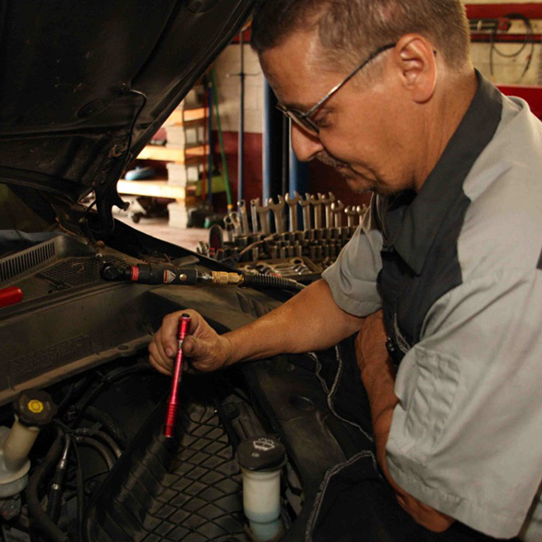 Kevin Hanks Sr. doing transmission work under the hood of a vehicle inside Wichita auto shop